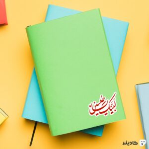 استیکر لپ تاپ لبیک حسین جان (ع) روی دفترچه